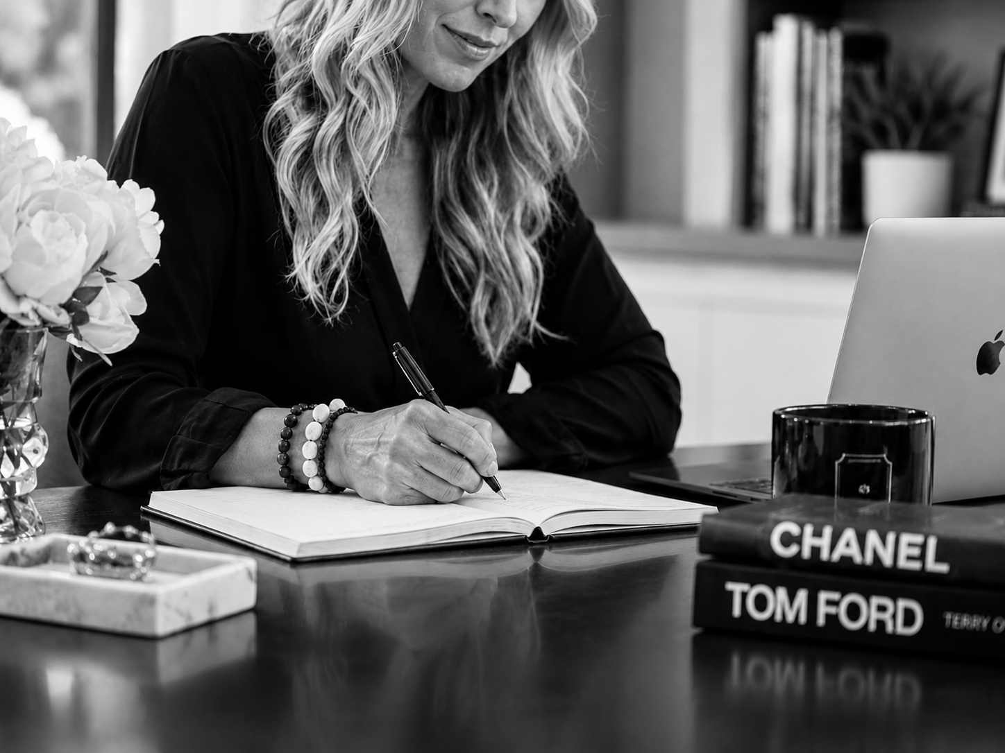 Black-and-white portrait of a woman writing at a desk in a modern office, reflecting a creative workspace.