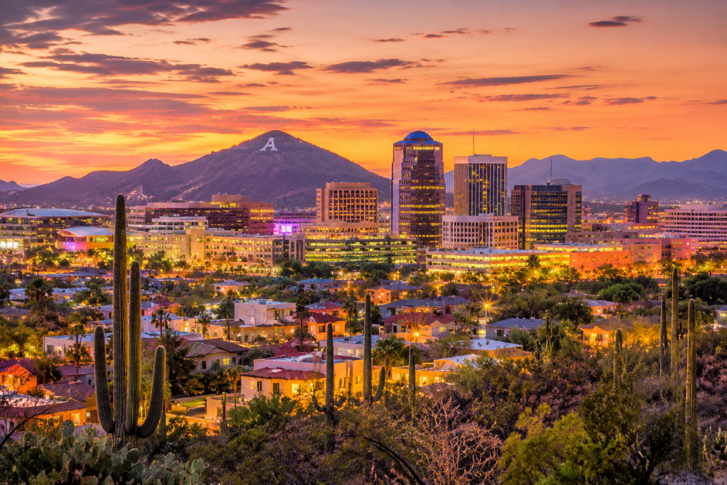 Tucson skyline at sunset, with downtown lights, desert landscapes, saguaro cacti, and mountains in the distance.