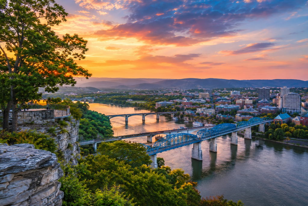 Chattanooga, Tennessee at sunset, overlooking the Tennessee River, downtown skyline, bridges, lush greenery and surrounding mountains.